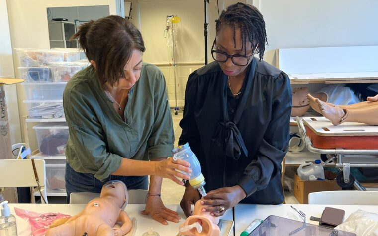 Deux personnes s’exercent à la ventilation au ballon sur une tête d’entraînement néonatale, un mannequin de nouveau-né posé à côté.