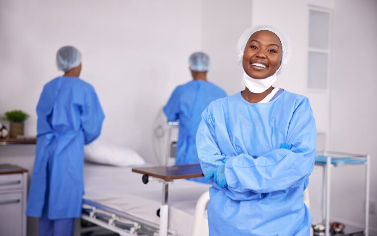 Soignante souriante en blouse, bras croisés, dans une chambre d’hôpital